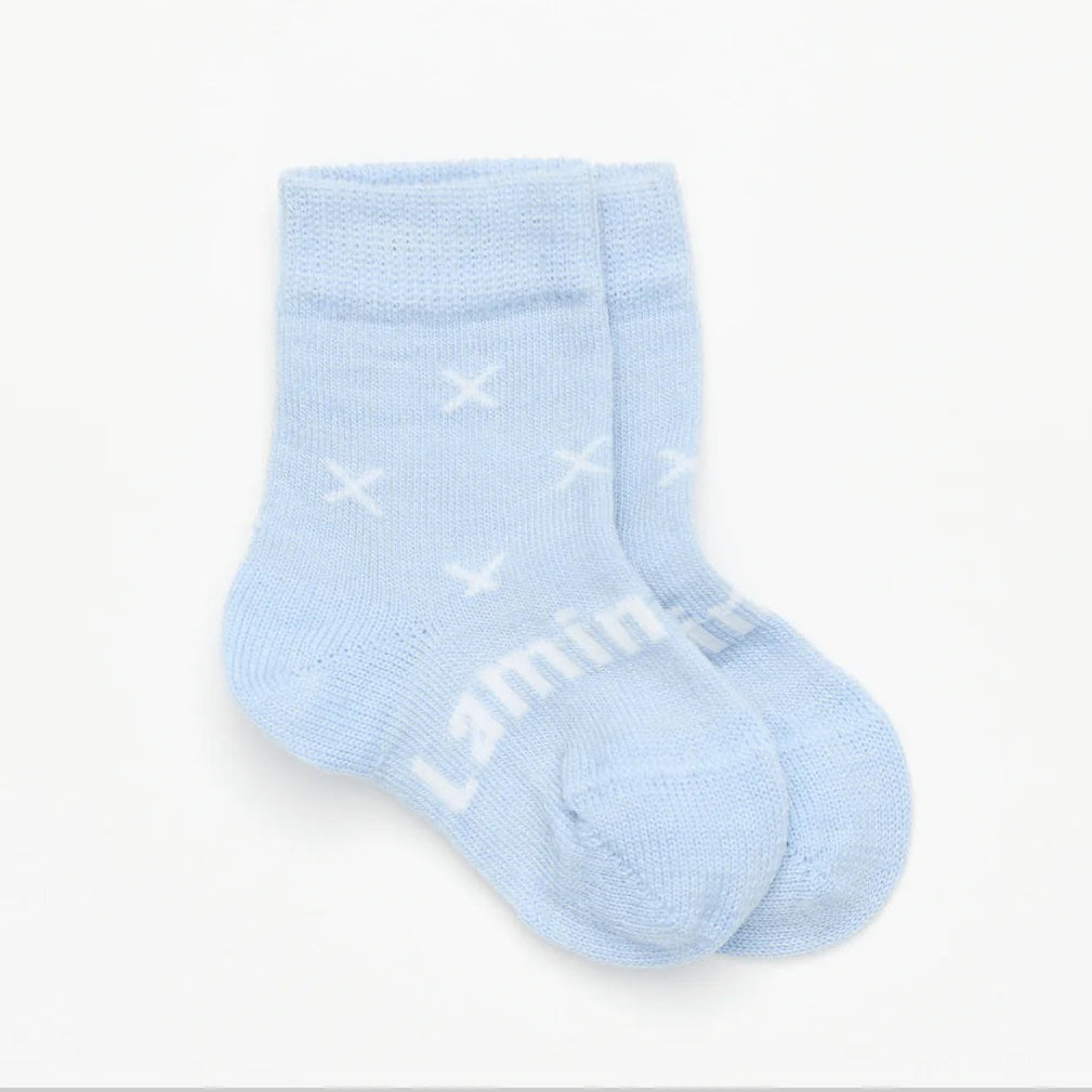 Light blue merino wool baby sock with white cross patterns on a light gray background