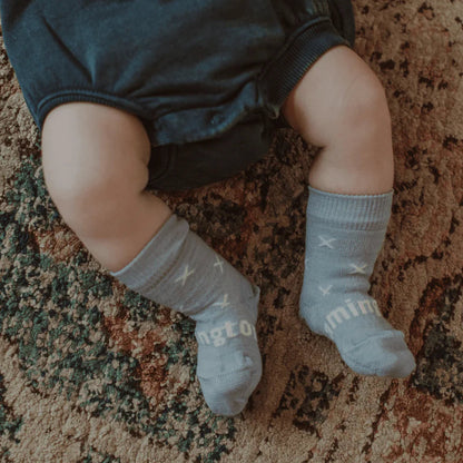 Baby legs wearing blue with white cross merino wool socks on a patterned carpet
