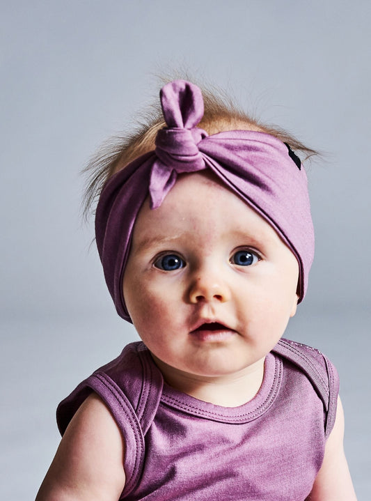 Baby wearing a mauve pink merino wool outfit and headband sitting on a gray background