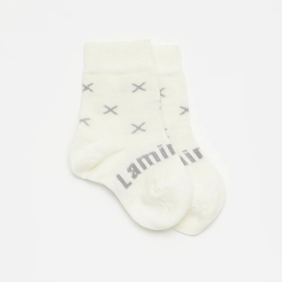 White merino wool baby sock with grey crosses and Lamington brand name on a light gray background