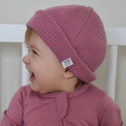 Baby wearing a pink merino wool rib hat sitting.