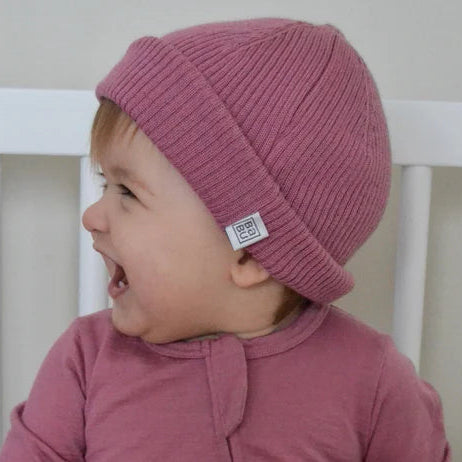 Baby wearing a pink merino wool rib hat sitting.