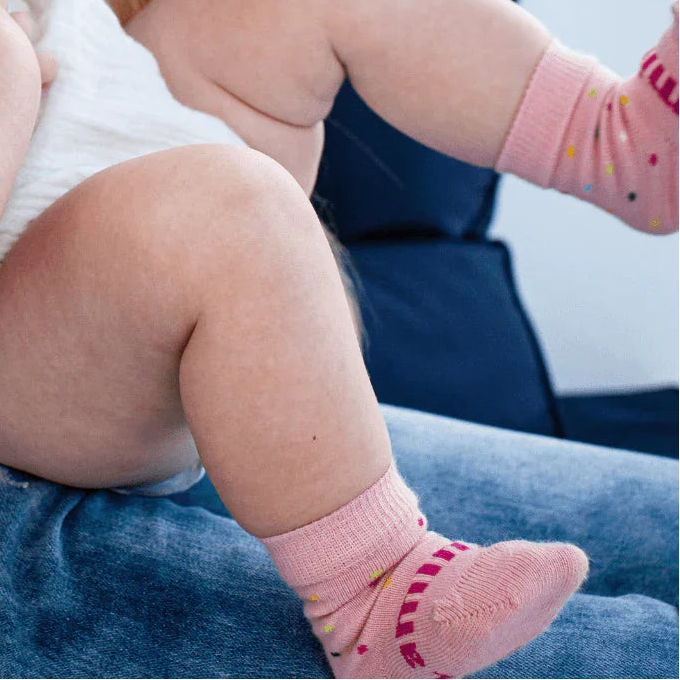 A baby wearing pink merino wool coloured spotted socks sits on a person's lap